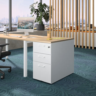 Lifestyle image of a white Buronomic Comfort desk-height pedestal with wire oak top under a desk